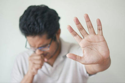 A man wearing glasses and a white shirt raises his hand